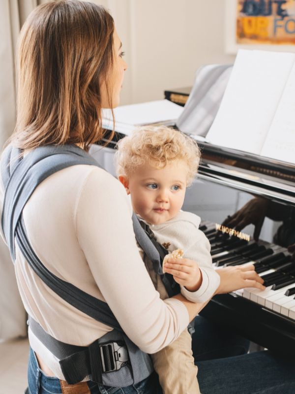 mama porteando mientras portea a su beb&eacute; tocando el piano usando el portabeb&eacute;s Mei Carrier